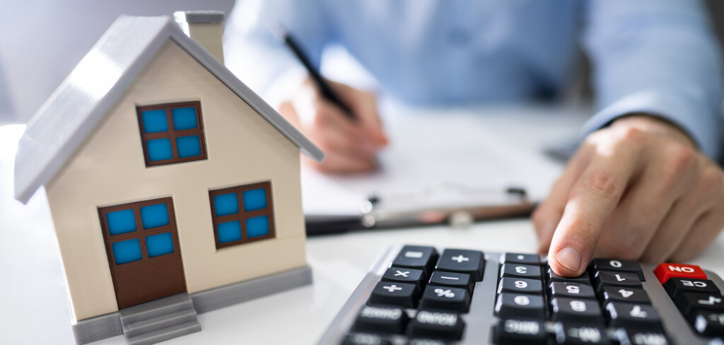 Close-up Of A Person Hand Calculating A Real Estate Property Tax On Wooden Desk