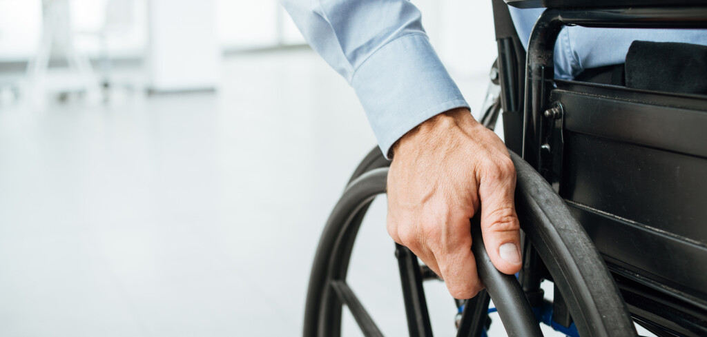 Businessman in wheelchair, hand on wheel close up, office interior on background