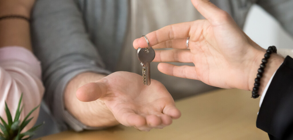 Close up of real estate agent giving keys to newlywed couple buying first home, young spouses becoming owners of new apartment or house, lovers start living together, purchasing shared property