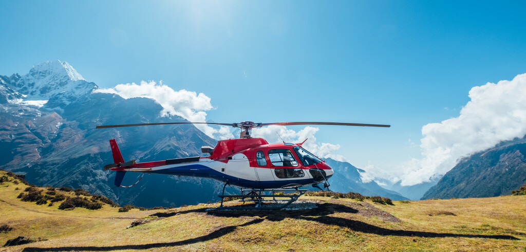 Civil helicopter landed in high altitude Himalayas mountains. Thamserku 6608m mountain on the background. Namche Bazaar, Nepal. Safety air transportation and travel insurance concept image.