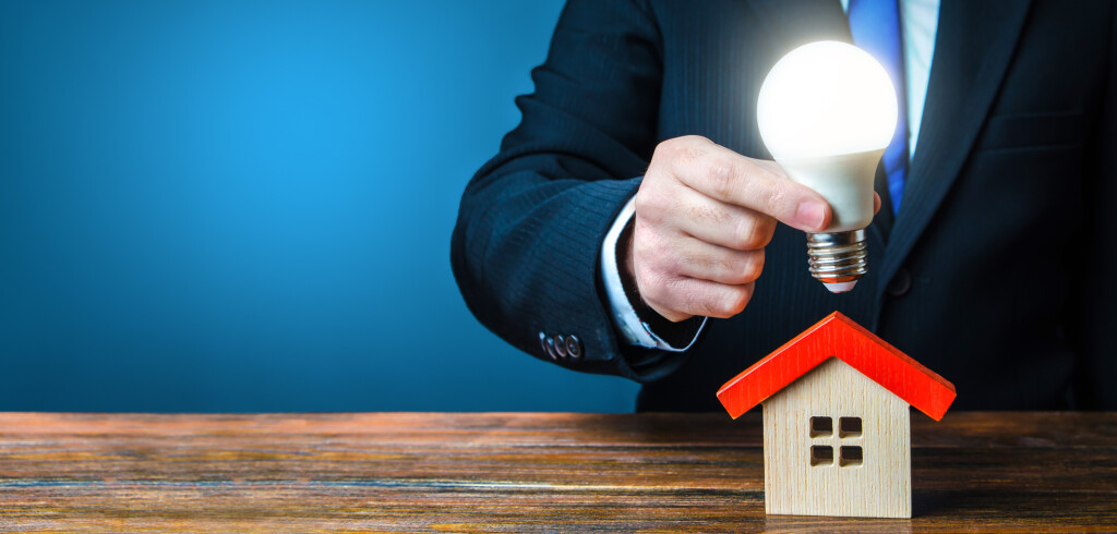 Man is holding a glowing light bulb over the house. Smart home concept. Provision of housing with electricity and communications. Deal contract with supply utilities companies. Pay electricity bills