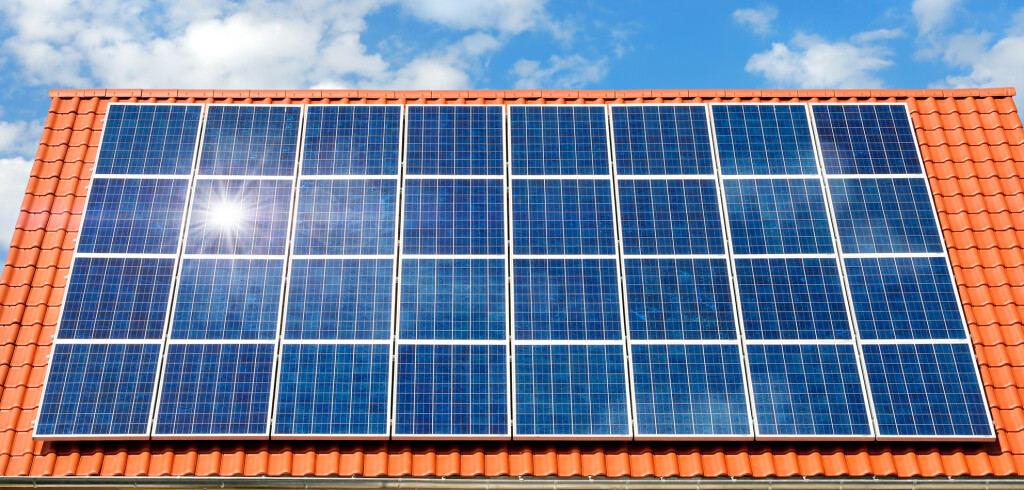 Roof with solar panel reflecting the sun, in the background a perfect sky with fluffy white clouds