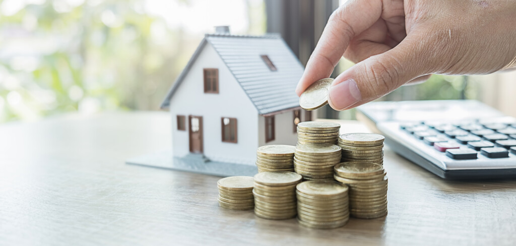 Saving money for house and real estate. Woman hand protecting on stack coins and house model on table.