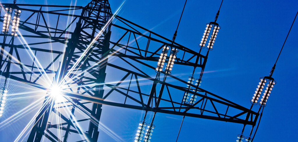 a high-voltage electricity pylons against blue sky and sun rays