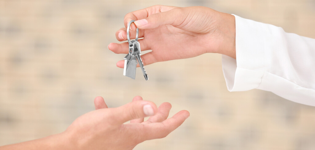 Estate agent giving key from new apartment to man on blurred background