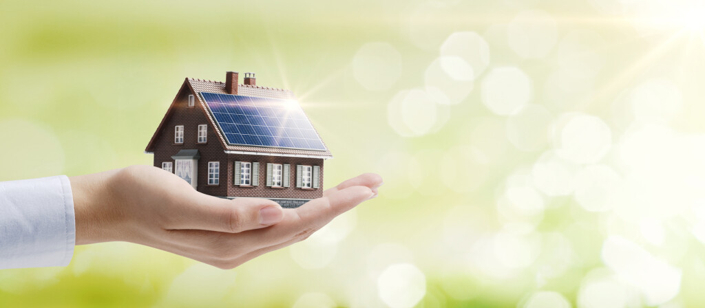 Hand holding an energy efficient model house with solar panels, ecology and sustainability concept