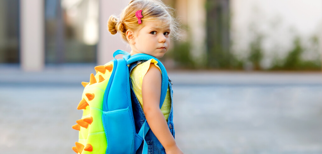 Cute little adorable toddler girl on her first day going to playschool. Healthy upset sad baby walking to nursery school. Fear of kindergarten. Unhappy child with backpack on city street, outdoors