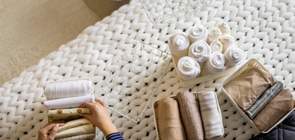 Modern housewife putting neatly folded towels, pillowcases, duvet covers into plastic metallic case boxes use Marie Kondo method storage organization. Woman making seasonal tidying up at home cupboard