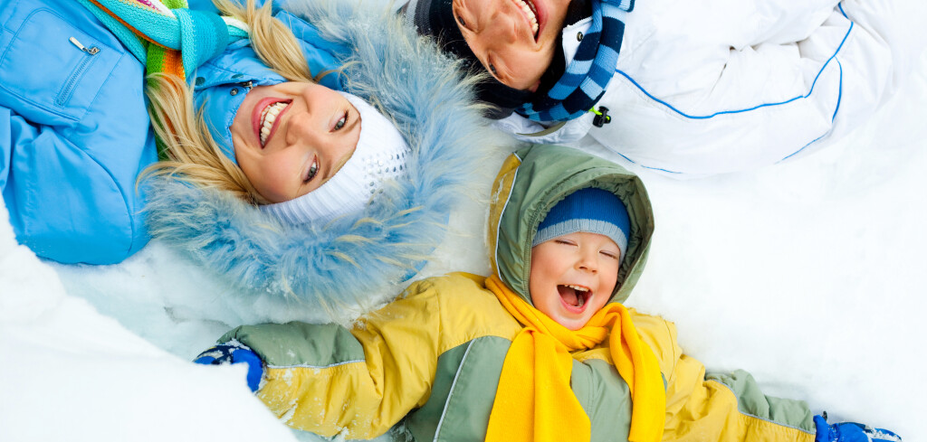 Young parents and their son wearing warm winter clothes lie on the snow