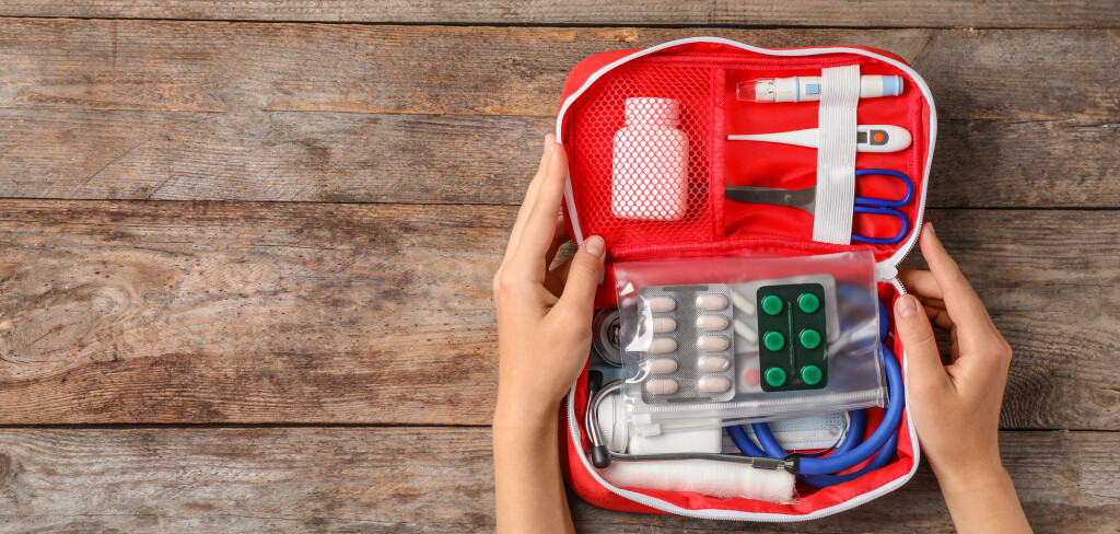 Woman holding first aid kit on wooden background, top view with space for text