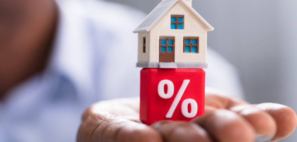 Close-up Of A Person's Hand Holding Miniature House On Red Percentage Block