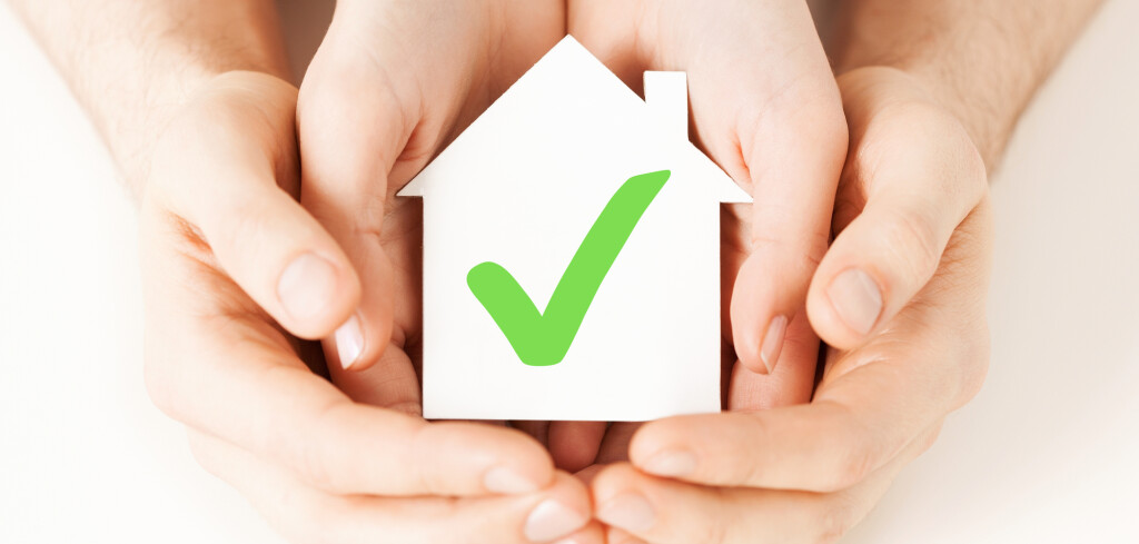 real estate and family home concept - male and female hands holding paper house with green check mark
