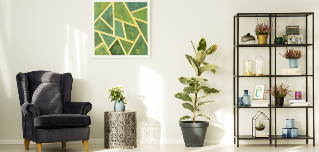 Elegant, black armchair in a reading corner of a bright interior with white walls and green decorations