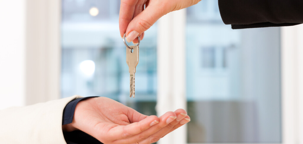 Young realtor is giving the keys to an apartment to the tenant, close-up on keys and hands