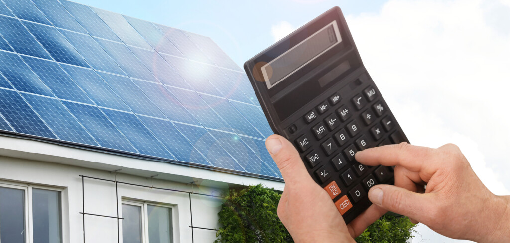 Man using calculator against house with installed solar panels. Renewable energy and money saving